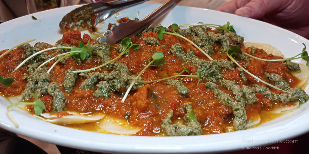 raw turnip ravioli stuffed with cashew cheese in a bed of pesto and roasted tomato sauce